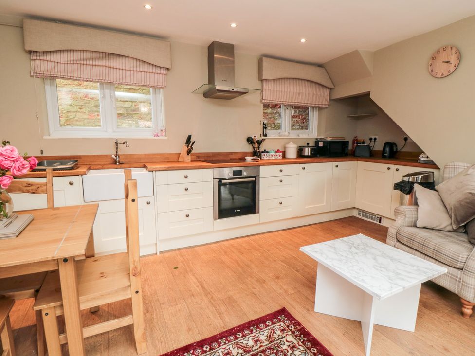 A kitchen with white cabinets wooden countertops a wooden dining table and chairs a small white coffee table and an armchair at Swainby Cottage in Swainby