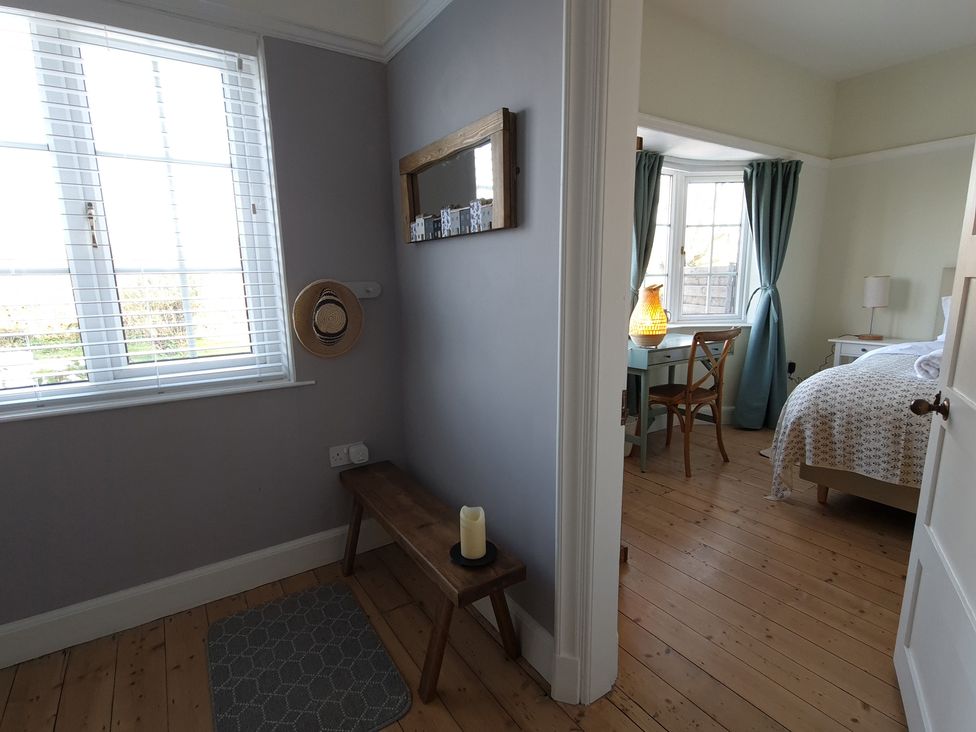 A hallway with a wooden bench and a candle next to a bedroom with a bed desk and a chair at Neuadd Wen in Benllech