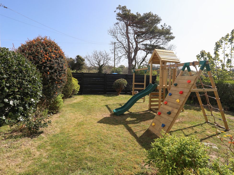 A garden with a wooden playset slide climbing wall and swings and bushes at Neuadd Wen in Benllech
