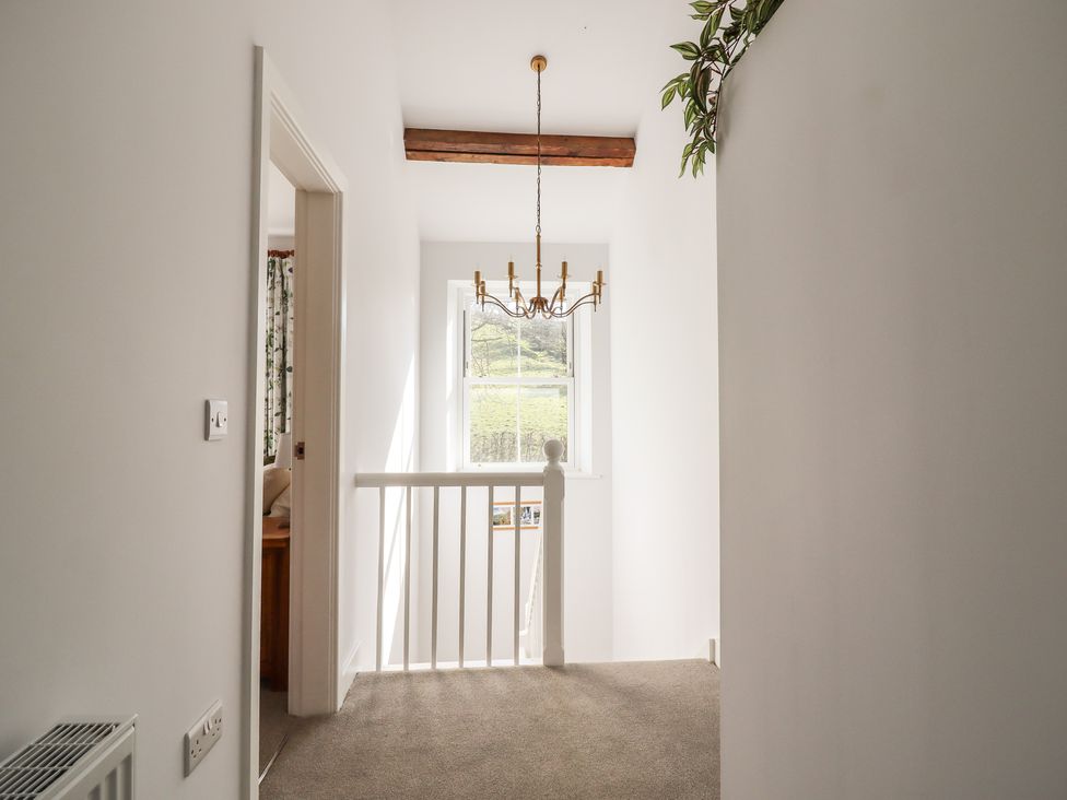A hallway with carpeted floor a white wooden banister a window with a view of greenery and a chandelier hanging from the ceiling at 1 Hull House Cottage in Hellifield