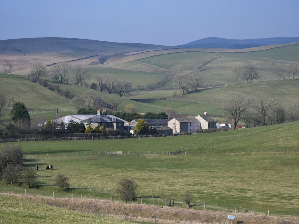A rural farmstead with stone buildings and fenced pastures with grazing cattle in a hilly landscape