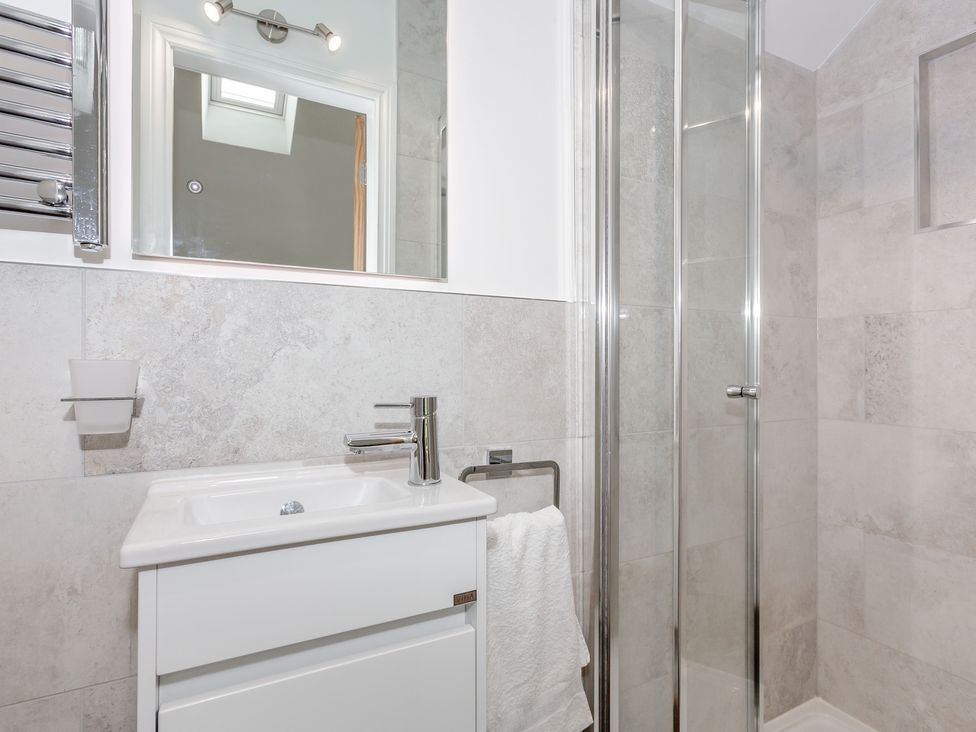 A bathroom with a sink, mirror, towel on a rack, and a glass shower enclosure at Pogles Wood Cottage in Grassington