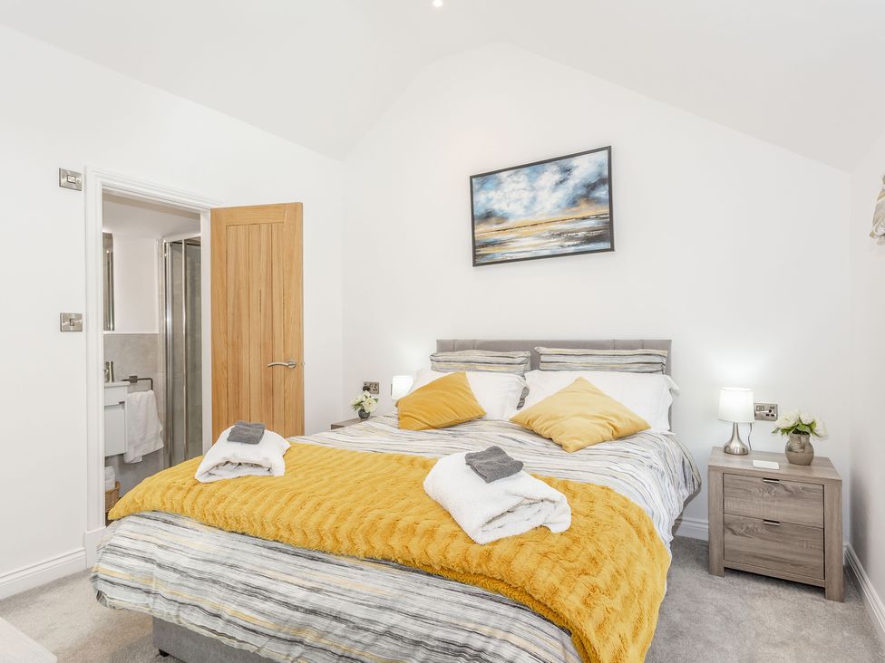 A bedroom with a bed with yellow and striped bedding bedside tables and an open door to a bathroom at Pogles Wood Cottage in Grassington