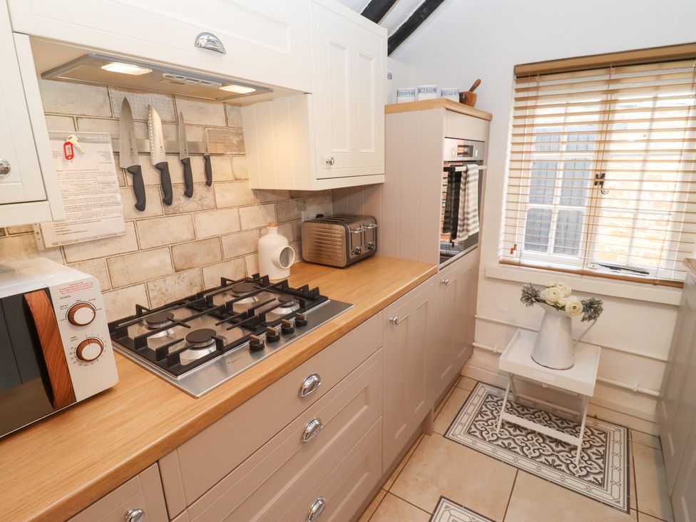 A kitchen with a gas stove microwave toaster knives on a magnetic strip and a window with blinds at Hobbes Cottage in Malmesbury