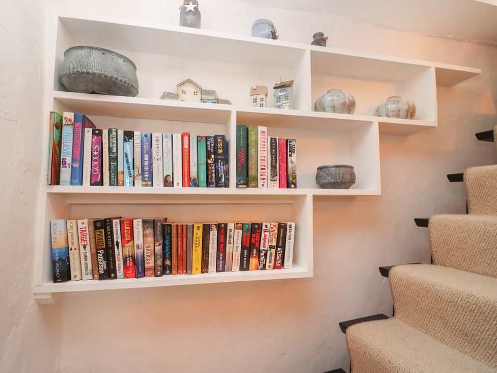A built in white bookshelf filled with books and decorative pots next to carpeted stairs at Hobbes Cottage in Malmesbury