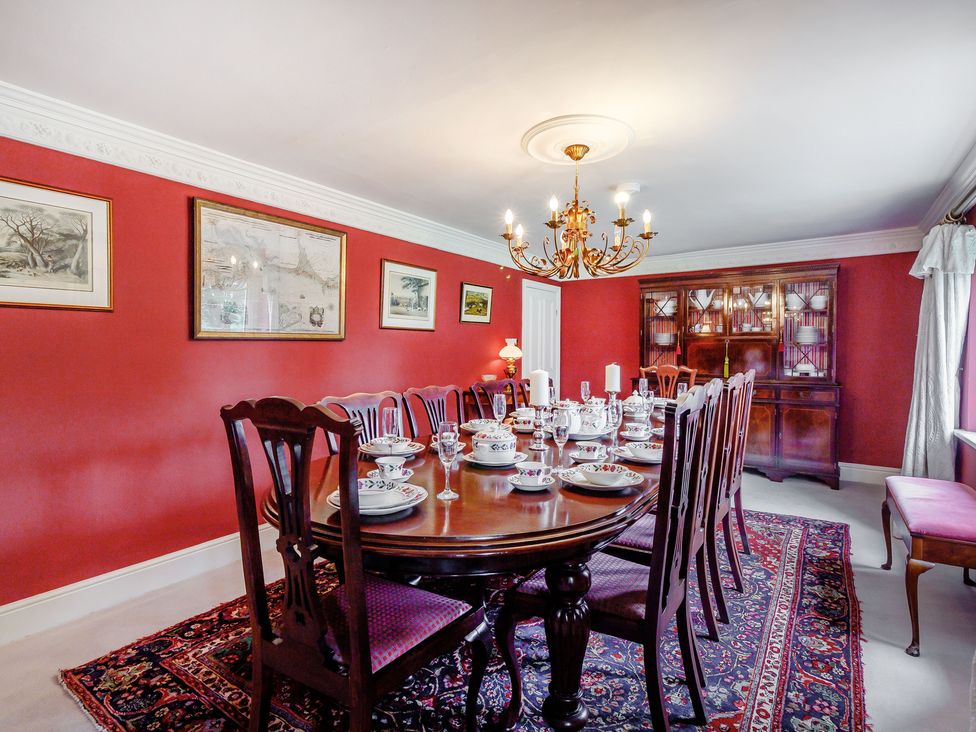 A dining room with a wooden table set with dishes and glassware surrounded by wooden chairs on a patterned rug at Fence House in Fence