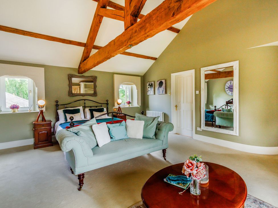 A bedroom with a bed and sofa under wooden ceiling beams and a round wooden table with flowers at Fence House in Fence