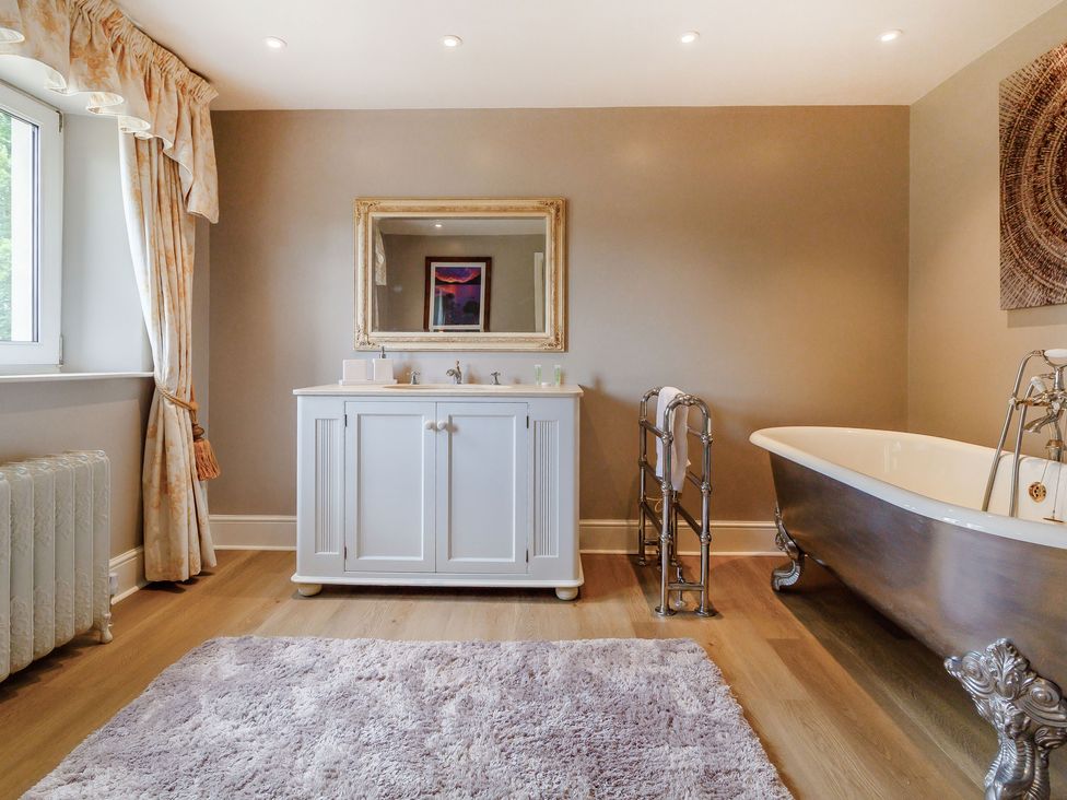 A bathroom with a white vanity and mirror a metal clawfoot bathtub a towel rack and a window with curtains at Fence House in Fence