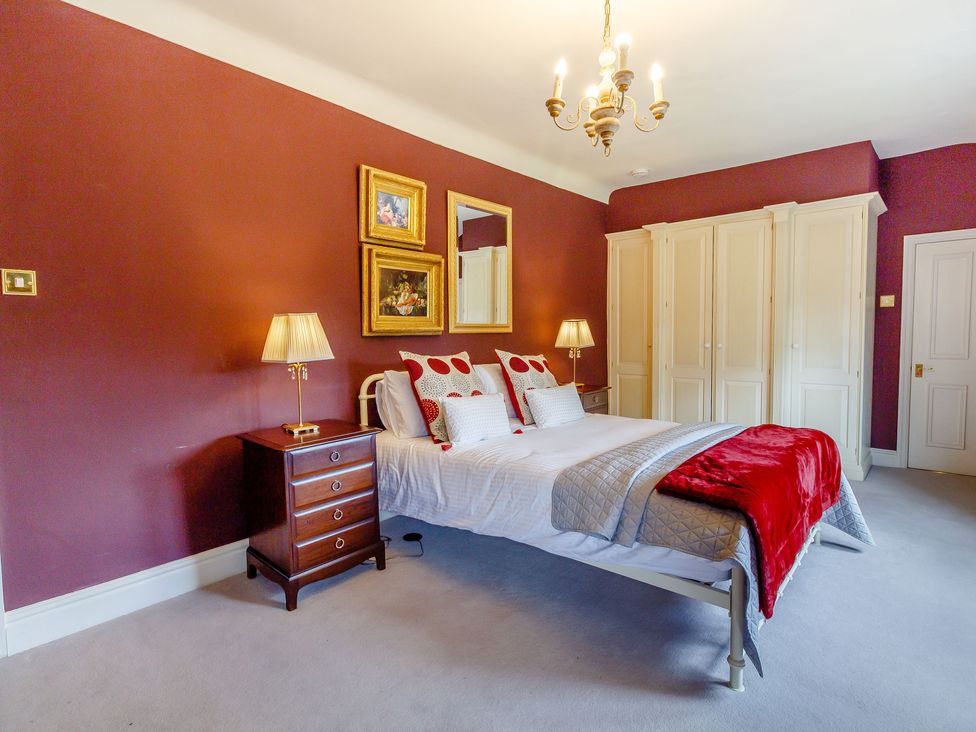 A bedroom with a bed bedside tables lamps paintings and a wardrobe at Fence House in Fence