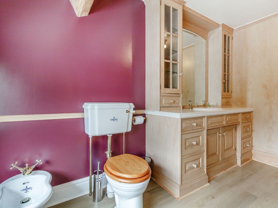 A bathroom with a toilet with wooden seat a bidet and a wooden vanity cabinet with mirrored doors at Fence House in Fence