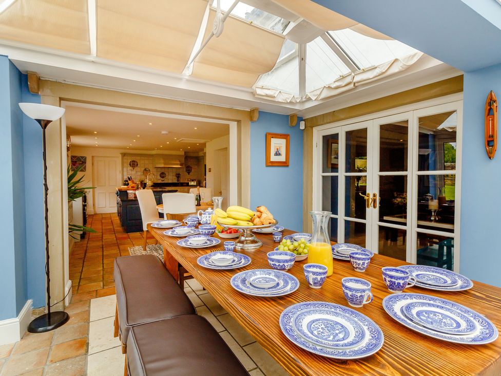 A dining area with a wooden table set with blue and white dishes and glassware under a skylight adjacent to a kitchen at Fence House in Fence