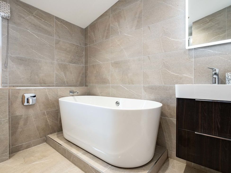 A bathroom with a white freestanding bathtub on a tiled platform and a sink with a dark cabinet at Artemis in Rock