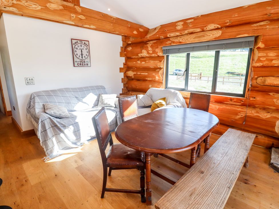 A dining area with wooden table chairs bench and sofas with cushions near window in a log cabin at Cedar Cabin Near Clifton Upon Teme
