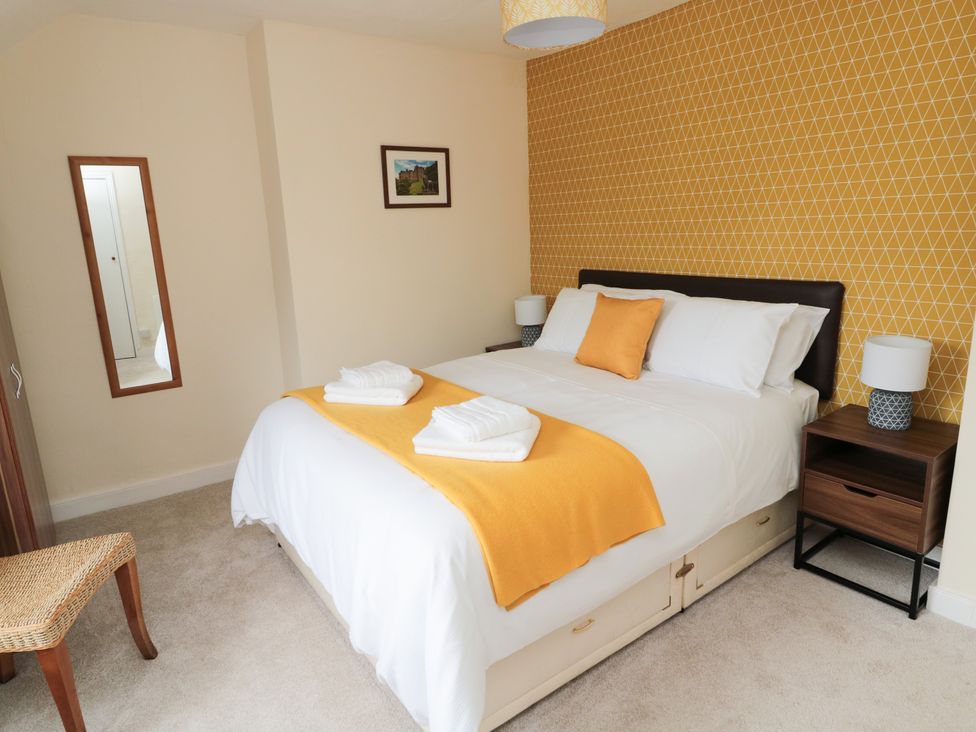 A bedroom with a double bed with white bedding and an orange runner and cushion bedside tables with lamps and a wall mirror at 1 Roddam Rigg Cottage Roddam near Wooler