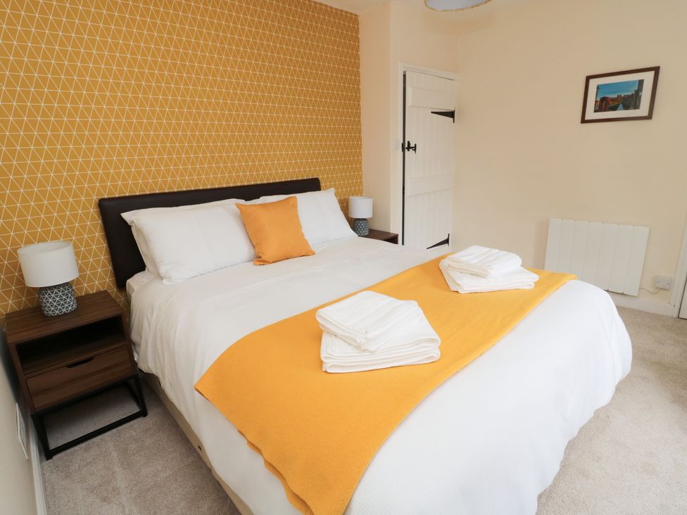 A bedroom with a double bed white bedding yellow blanket and cushion bedside tables with lamps at 1 Roddam Rigg Cottage in Roddam near Wooler