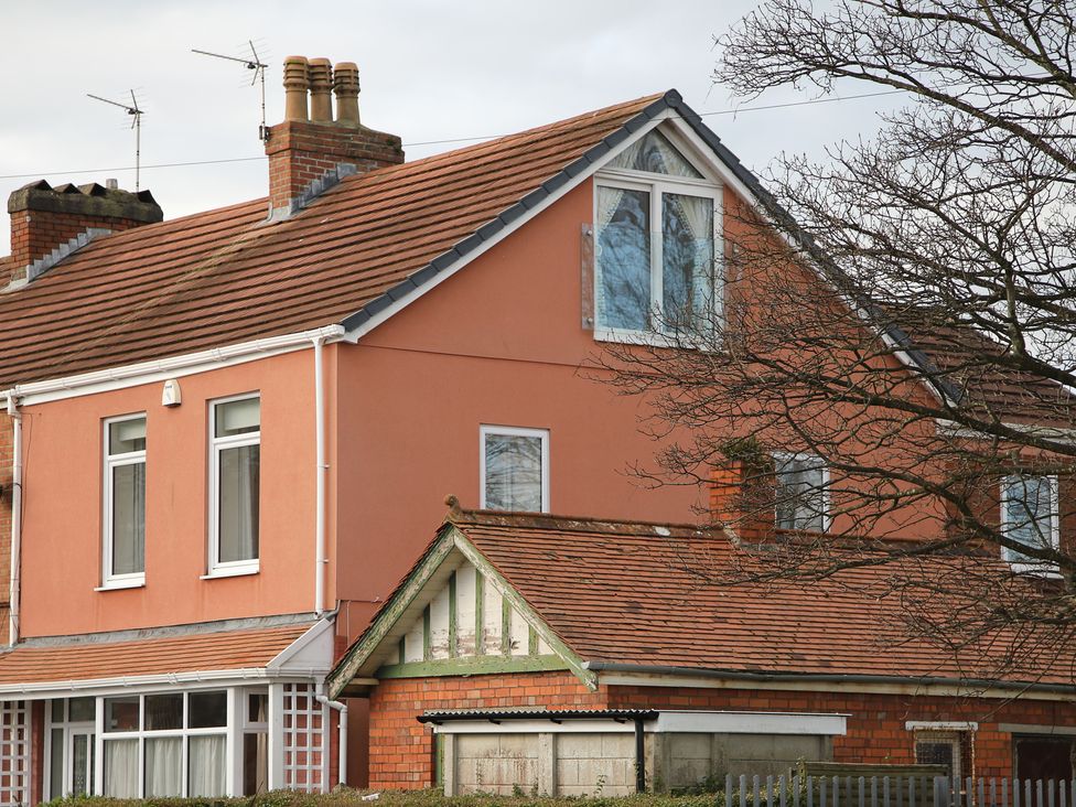 A two-story house with orange walls and a red tiled roof with chimneys and windows and a bare tree in front at The Headlands - Gower in The Mumbles