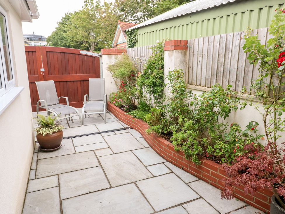 A patio with two chairs a potted plant a flower bed and a wooden gate at The Headlands - Gower in The Mumbles