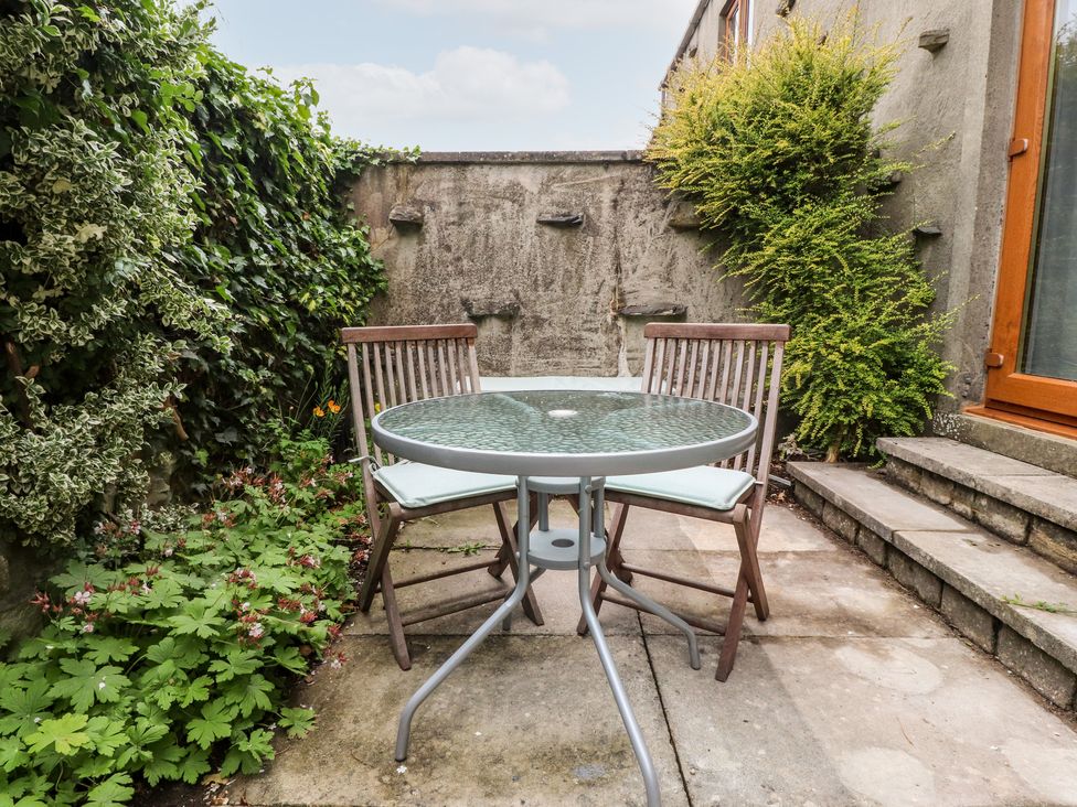 A small outdoor patio with a glass table and two wooden chairs surrounded by plants at Top House in Settle