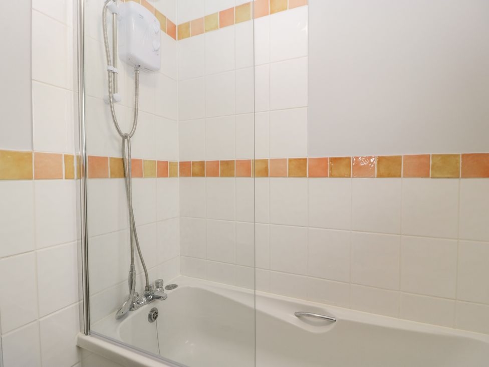 A bathroom with a bathtub a showerhead and white tiles with an orange border at Wren Cottage in Weymouth