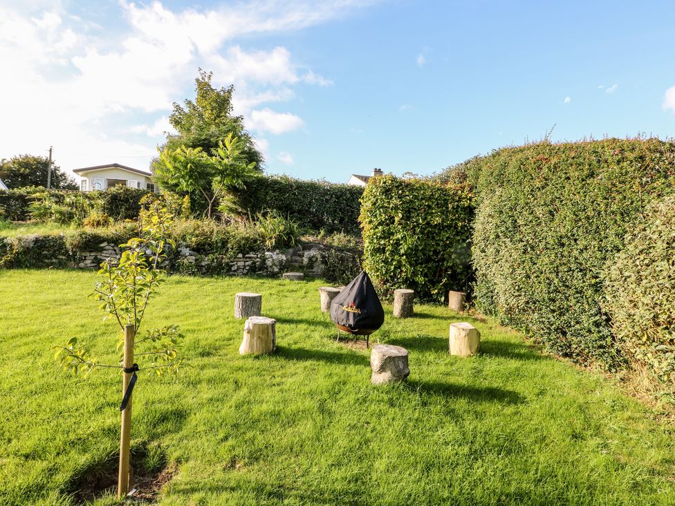 An outdoor garden area with logs arranged in a circle around a covered fire pit at Tegfryn Bach in Llangoed near Beaumaris