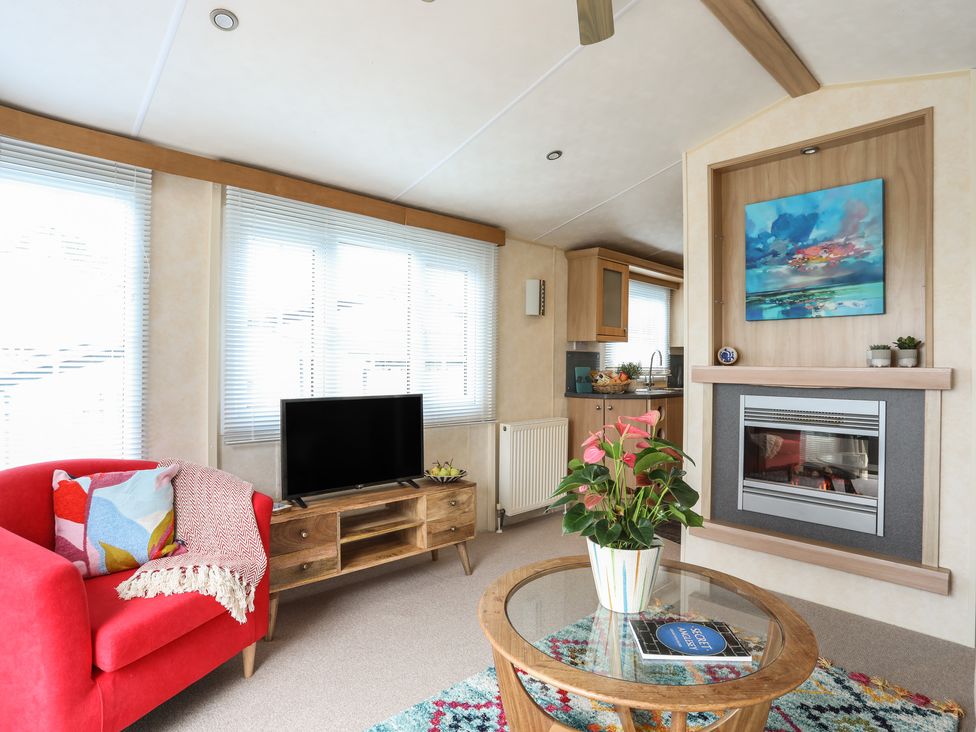 A living room with a red armchair a television on a wooden stand a fireplace and a glass coffee table with a plant at Tegfryn Bach Llangoed near Beaumaris