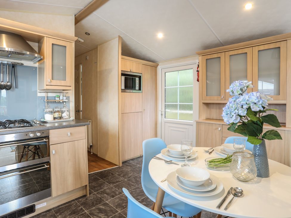 A kitchen with light wood cabinets a dining table set with plates bowls glasses and cutlery blue chairs and a vase of flowers at Tegfryn Bach in Llangoed near Beaumaris