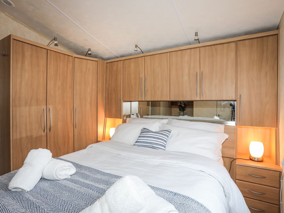 A bedroom with a double bed surrounded by wooden wardrobes and bedside tables with lamps at Tegfryn Bach in Llangoed near Beaumaris