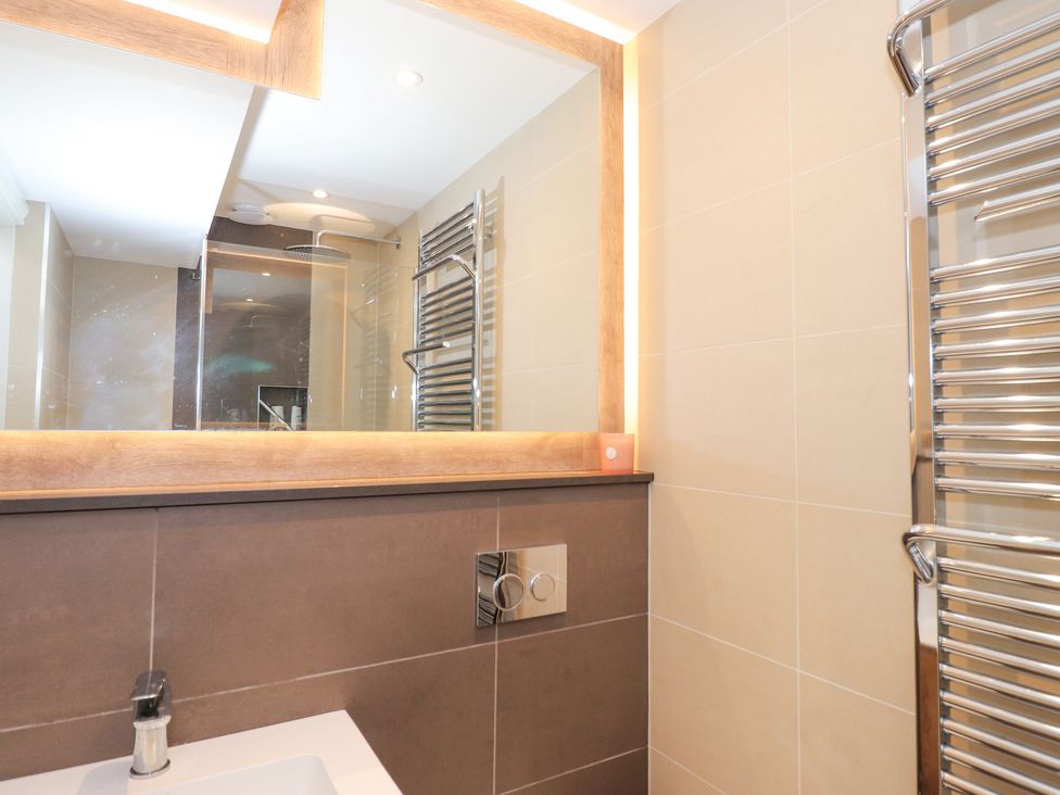 A bathroom with a sink faucet a large mirror a chrome towel radiator and a shower area at Rydal Suite Ambleside