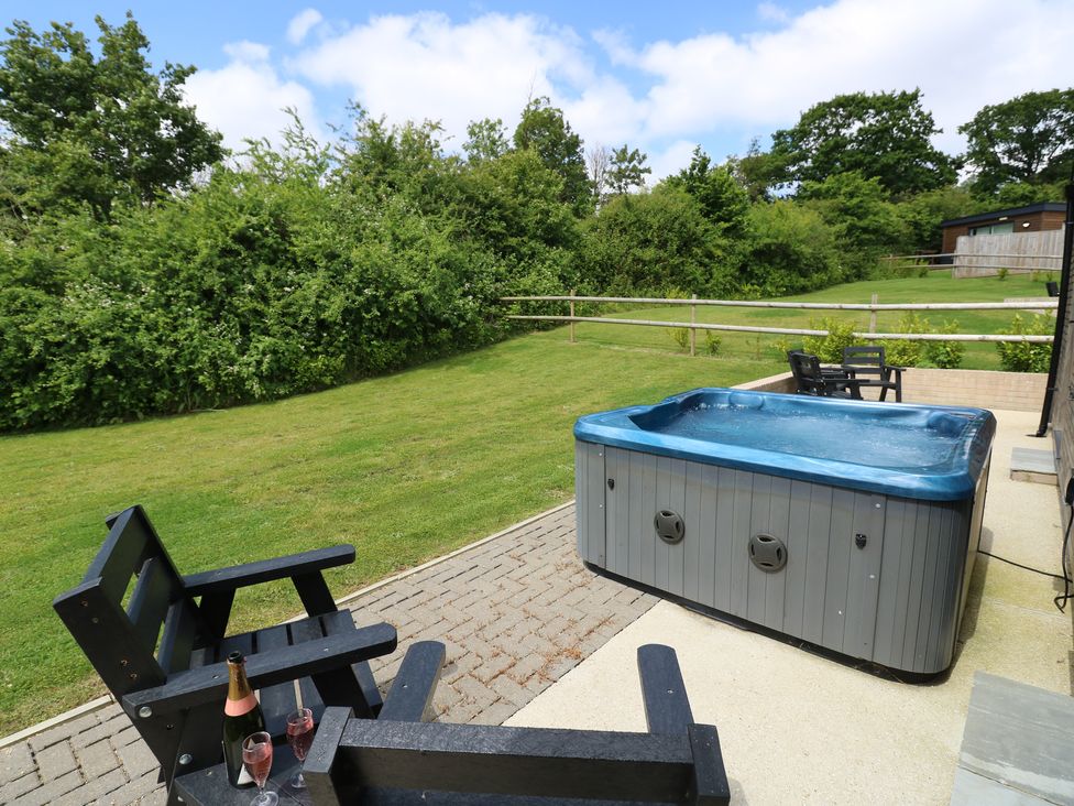 An outdoor area with a hot tub black wooden chairs a bottle of sparkling wine two glasses and a grassy fenced garden at Cava in Seaview