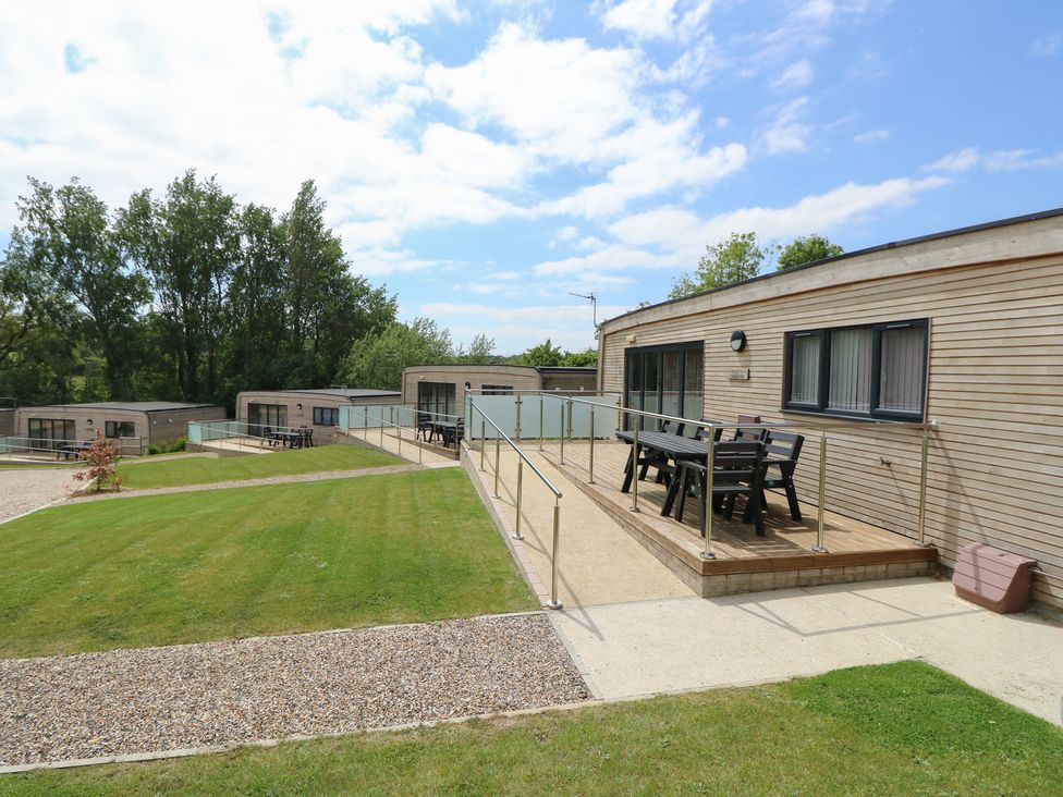 A group of modern wooden lodges with outdoor seating areas and railings surrounded by grass and trees at Cava in Seaview