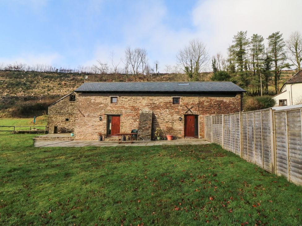 A stone cottage with two wooden doors and a skylight surrounded by grass and fencing at Red Deer Cottage in Wheddon Cross