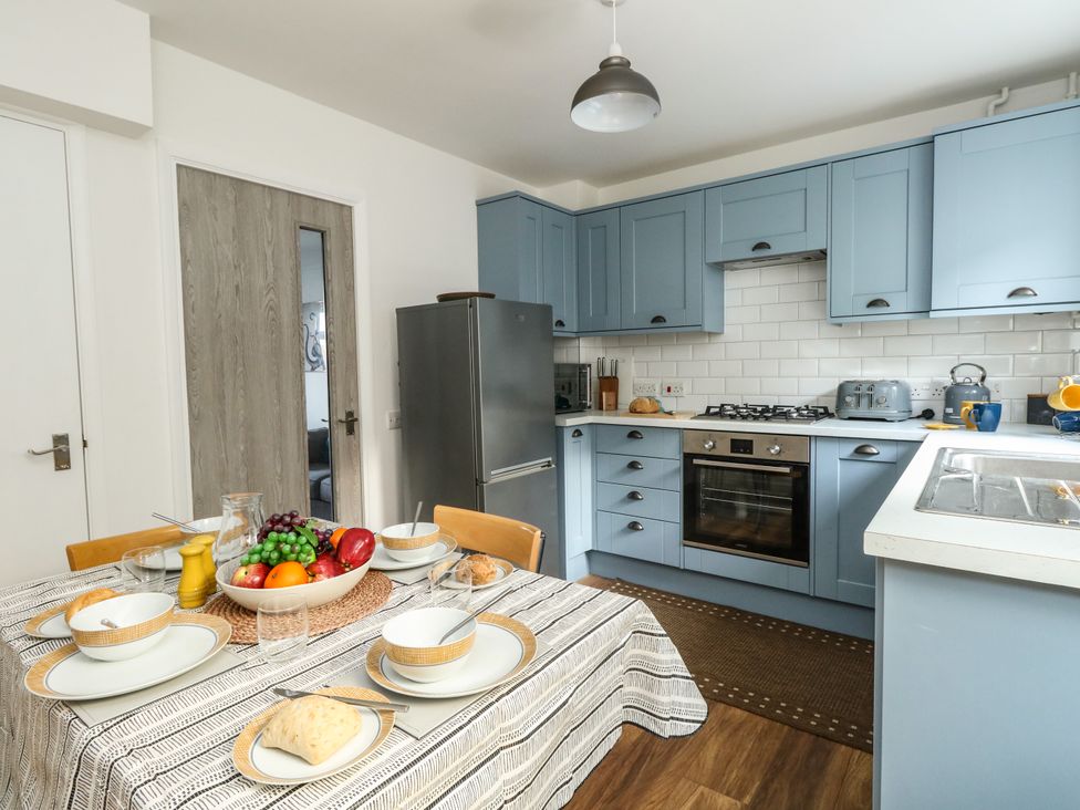 A kitchen with blue cabinets a dining table set with dishes and fruit at Little Tern Brewers Quay Harbour