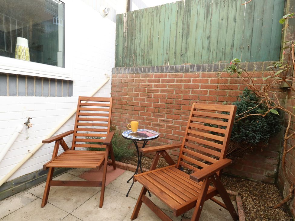 Two wooden chairs around a small round table with a yellow cup on it in an outdoor patio area with brick and green wooden fences at Little Tern Brewers Quay Harbour