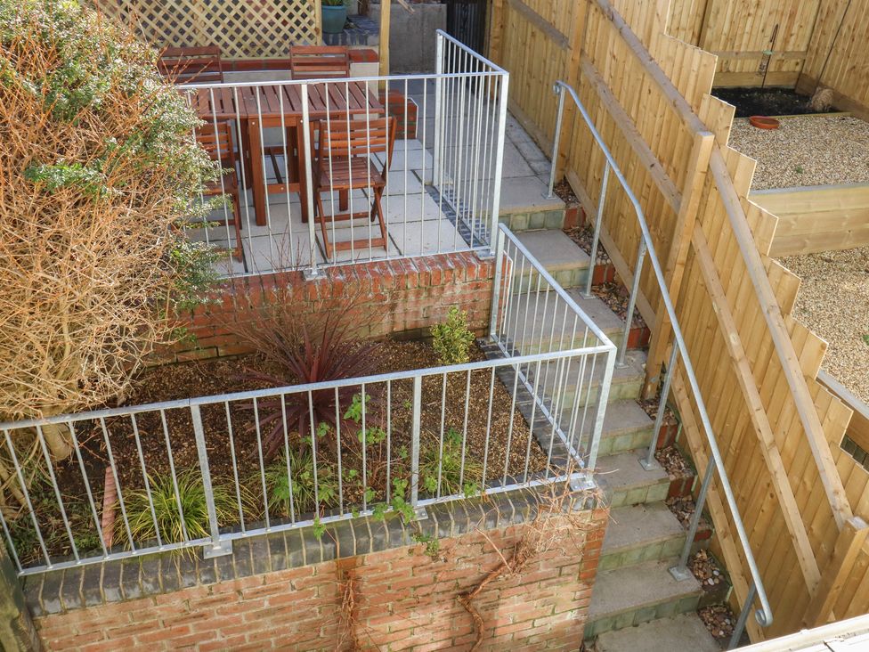 A backyard with a raised patio area with wooden dining furniture a small garden with plants and a staircase with metal railings at Little Tern Brewers Quay Harbour