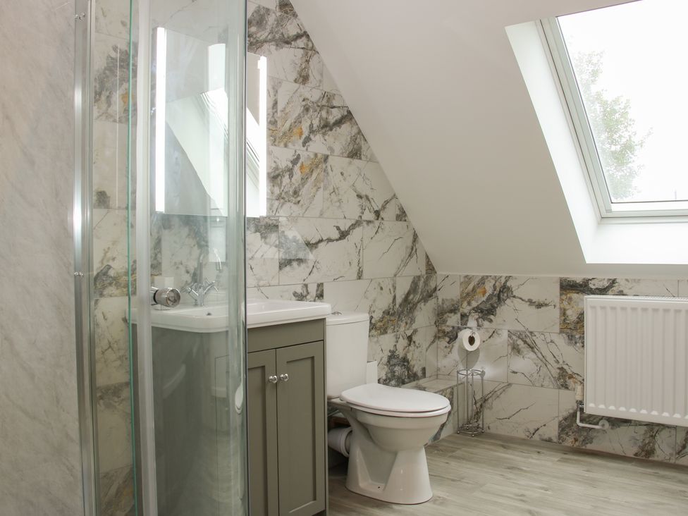 A bathroom with a toilet sink cabinet glass shower and a skylight at Holly Lodge in Forden near Montgomery
