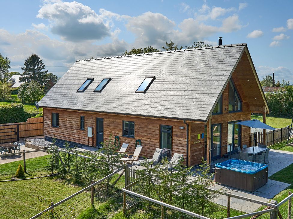 A wooden house with a patio featuring a hot tub chairs and a dining table with an umbrella at Holly Lodge in Forden near Montgomery