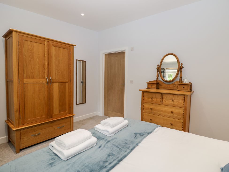 A bedroom with wooden wardrobe and dresser with mirror and towels on the bed at Stag Cottage in Lytchett Matravers