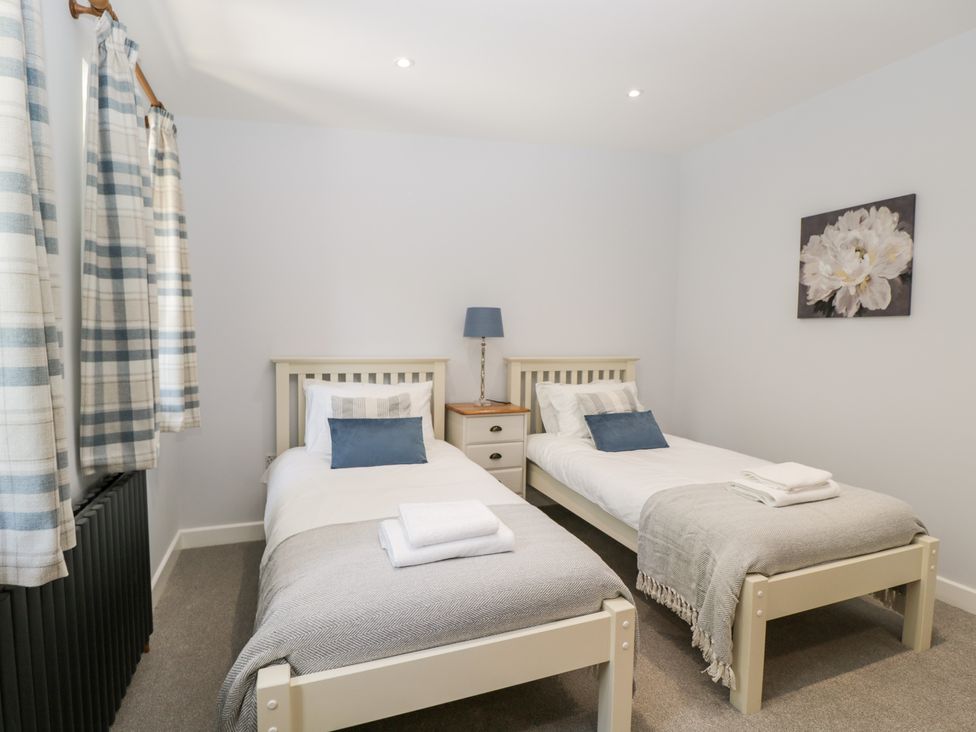 A bedroom with two single beds a nightstand with a lamp and a flower painting on the wall at Stag Cottage in Lytchett Matravers