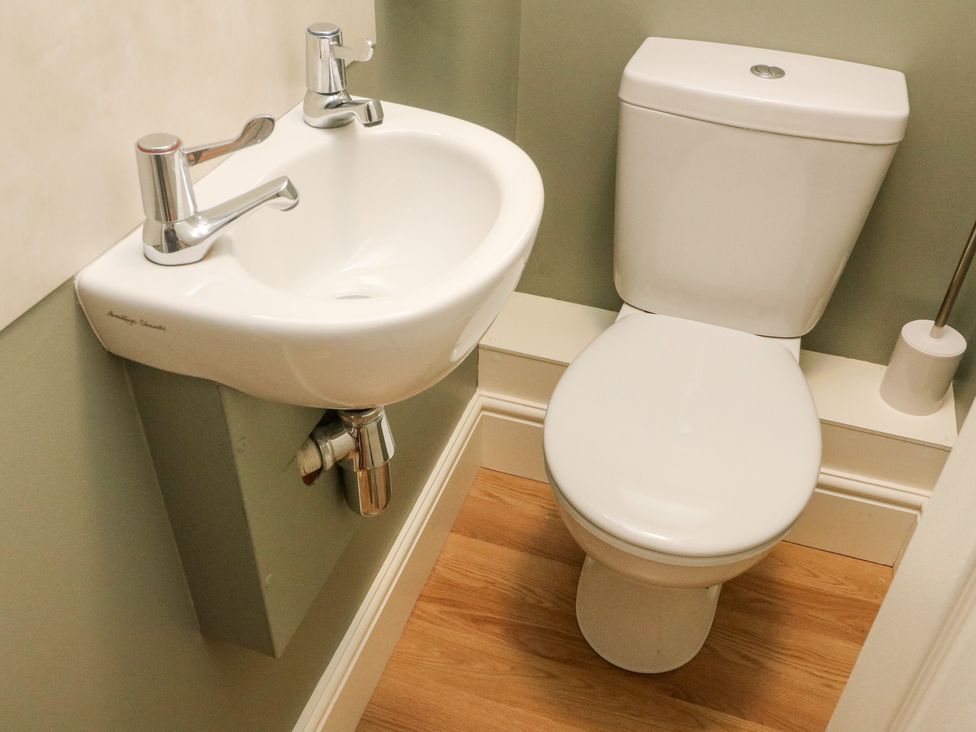A bathroom with a toilet and a small sink with two faucets at Heanor House in Leyburn