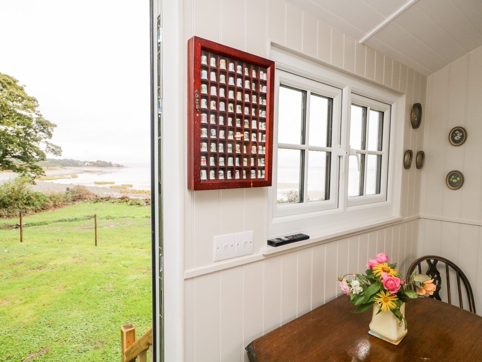 A dining area with a wooden table and flower vase by a window with a remote and a wall display of collectible thimbles at Seashore Shepherds Hut @ Moat Farm Aldingham near Ulverston
