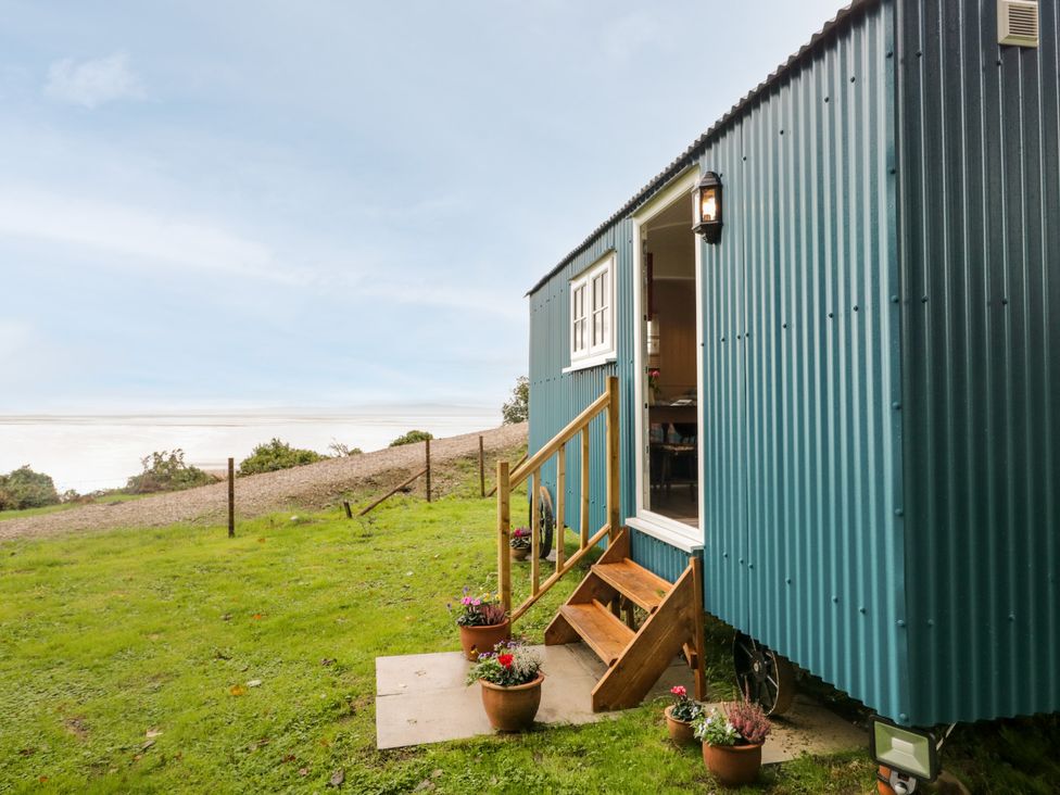 A blue shepherds hut with wooden steps and flower pots on grass at Seashore Shepherds Hut @ Moat Farm in Aldingham near Ulverston