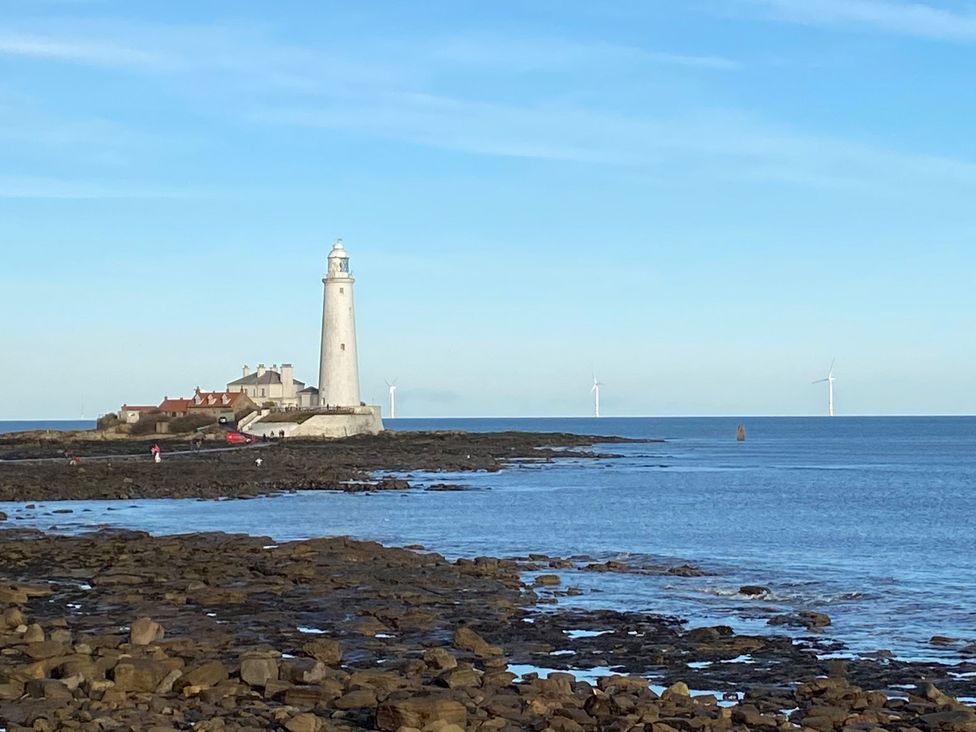 A coastline with a lighthouse on a rocky shore and wind turbines in the sea at Studio 51 @ Tynemouth in Tynemouth