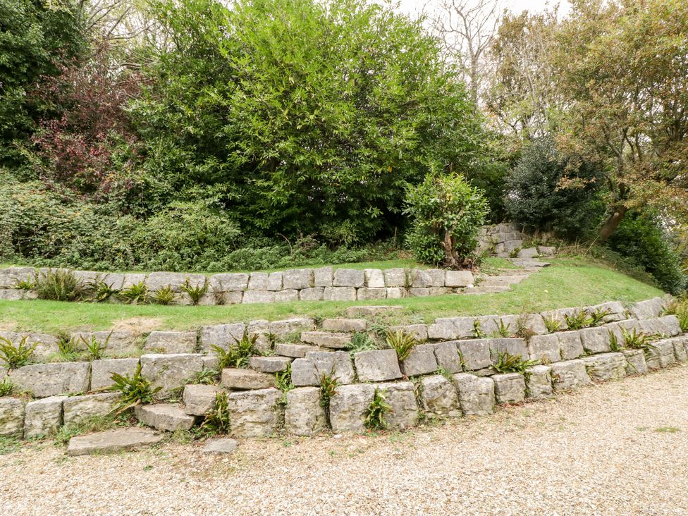 An outdoor area with stone retaining walls stone steps grass and trees at The Studio - Arne in Arne near Stoborough