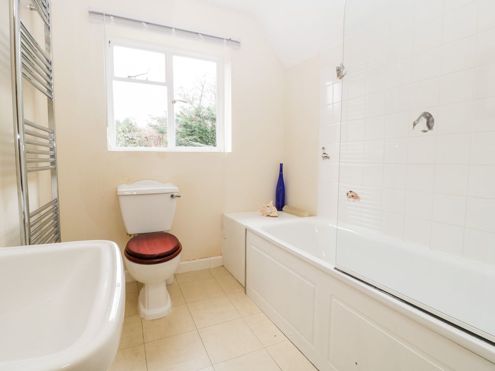A bathroom with a toilet, sink, bathtub, towel rail, and window at The Studio - Arne in Arne near Stoborough
