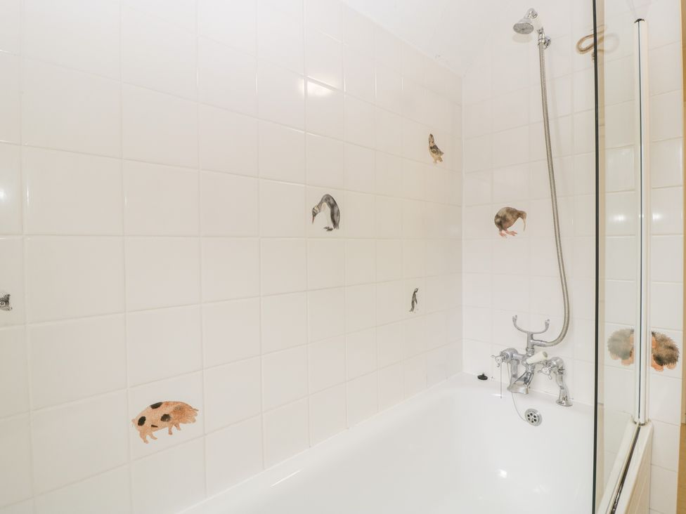 A bathroom with a bathtub and shower head above it with animal illustrations on the white tiled wall at The Studio - Arne in Arne near Stoborough
