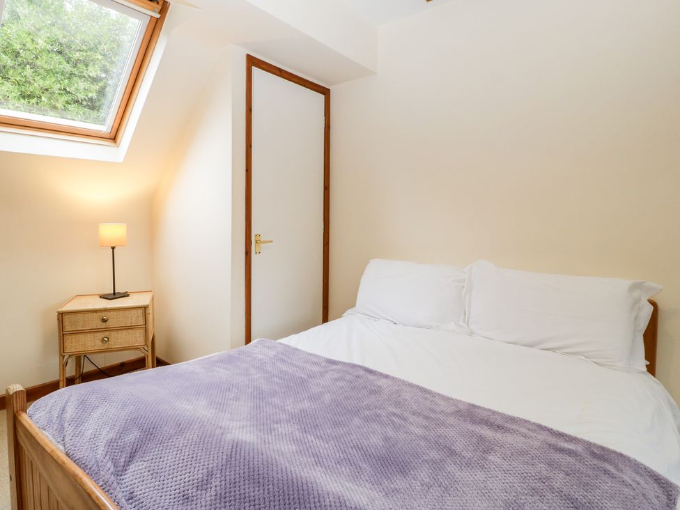 A bedroom with a bed covered with white sheets and a purple blanket a bedside table with a lamp a door and a window in the ceiling at The Studio - Arne in Arne near Stoborough