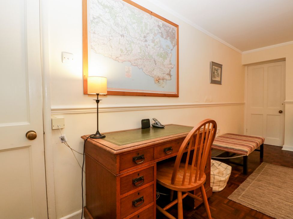 A room with a wooden desk, chair, lamp, map on wall, bench with striped cushion and a door at The Studio - Arne in Arne near Stoborough