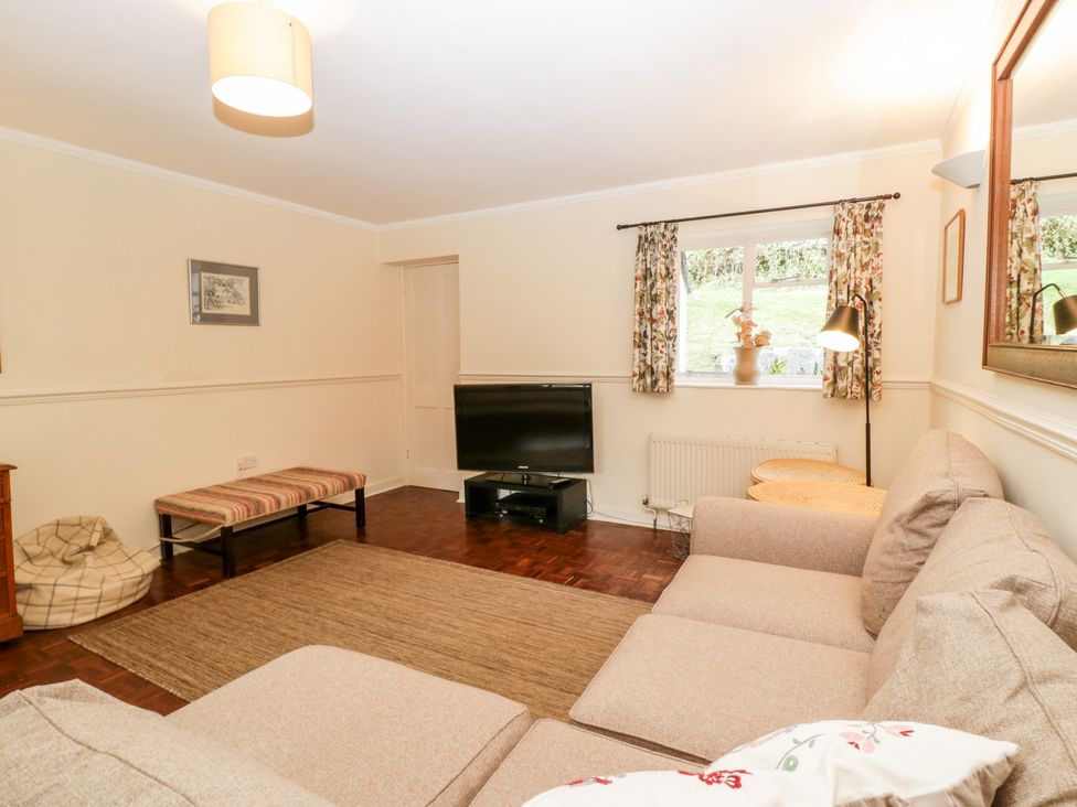 A living room with a beige sectional sofa a television on a stand a window with floral curtains and a floor lamp at The Studio - Arne near Stoborough