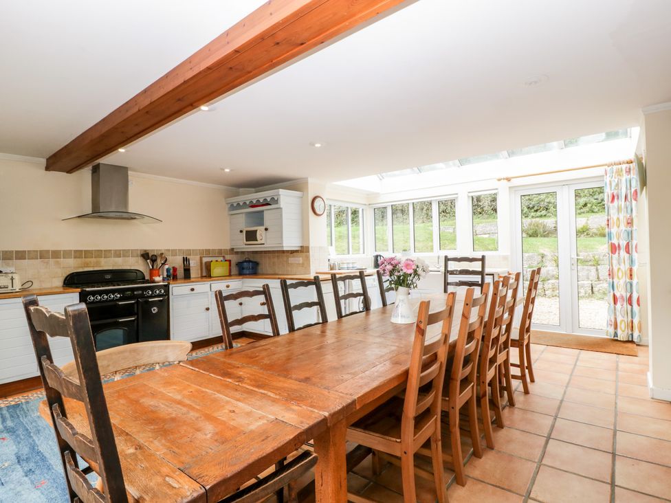 A kitchen and dining area with a long wooden table and multiple chairs a stove microwave and large windows at The Studio - Arne in Arne near Stoborough