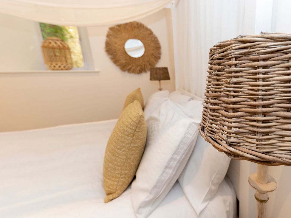 A bedroom with a bed with white sheets and pillows with woven cushions and a wicker lamp at Bishops Retreat in Ventnor